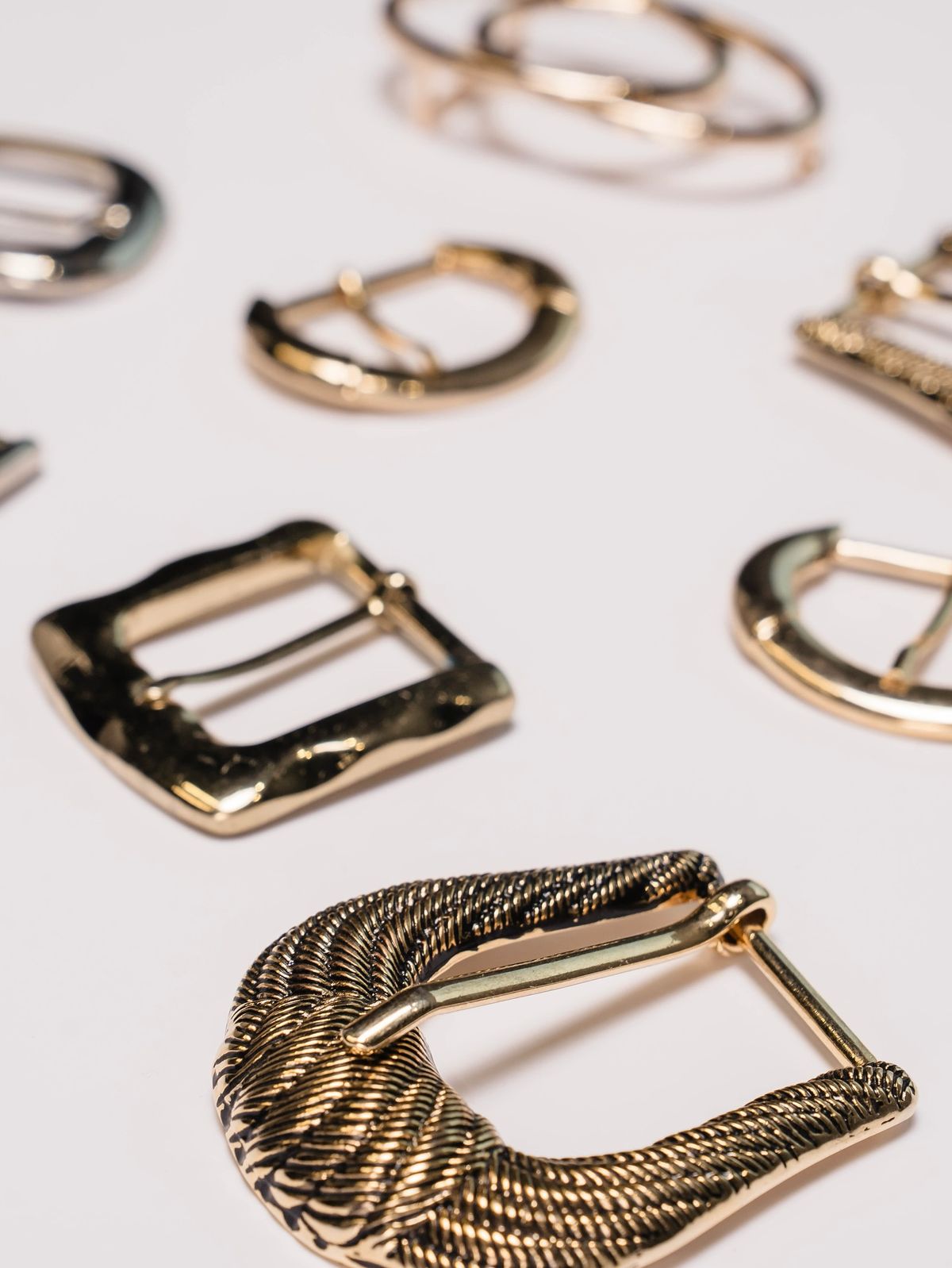 Gold belt buckles laid out on a pale studio surface